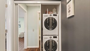 A laundry room with two stacked front-loading washing machines, a white door, and a hallway leading to another room. - Bright, Beautiful & Dog Friendly Steps to Old Town (Fort Collins)