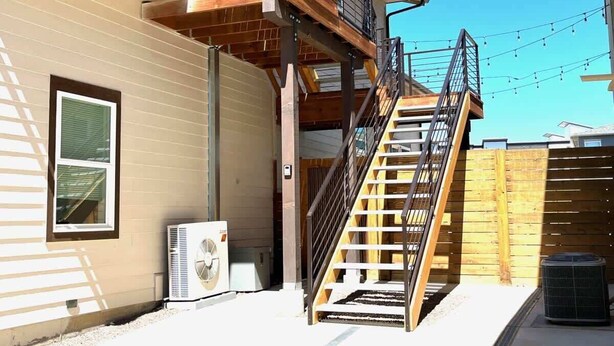 A residential building with a wooden deck, a staircase leading to a balcony, and a window with blinds. - Bright, Beautiful & Dog Friendly Steps to Old Town (Fort Collins)