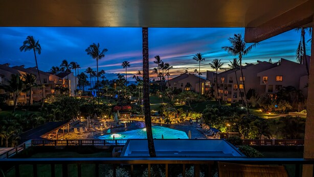 Un complexe hôtelier doté d’une piscine, de palmiers et de bâtiments illuminés au crépuscule.