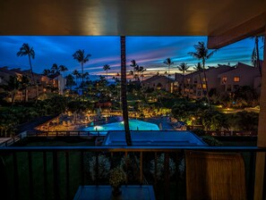 A resort with a pool, palm trees, and illuminated buildings at dusk. - Kamaole Sands 5307 condo with ocean view. Updated in August 2026. Split AC. (Kihei)