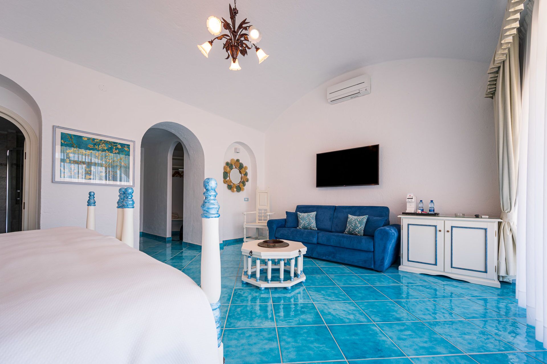 Een hotelkamer met een bed, een blauwe bank, een televisie en een klein tafeltje.