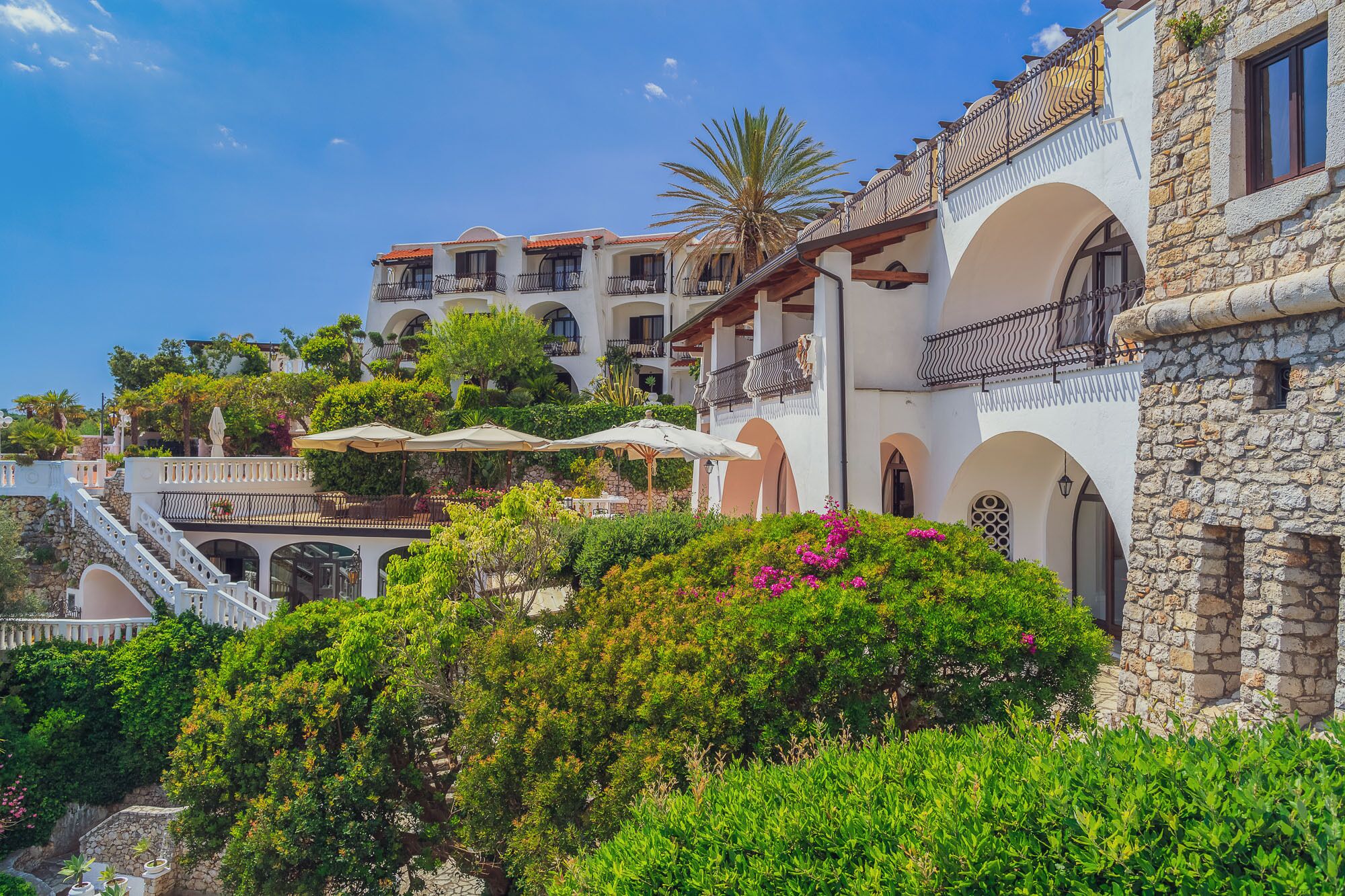 A multi-story building with balconies, stone walls, and lush greenery.