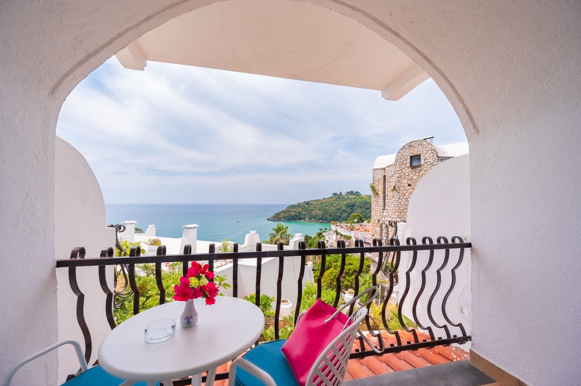 Un balcon avec vue sur la mer, un bâtiment en pierre et un mur blanc.