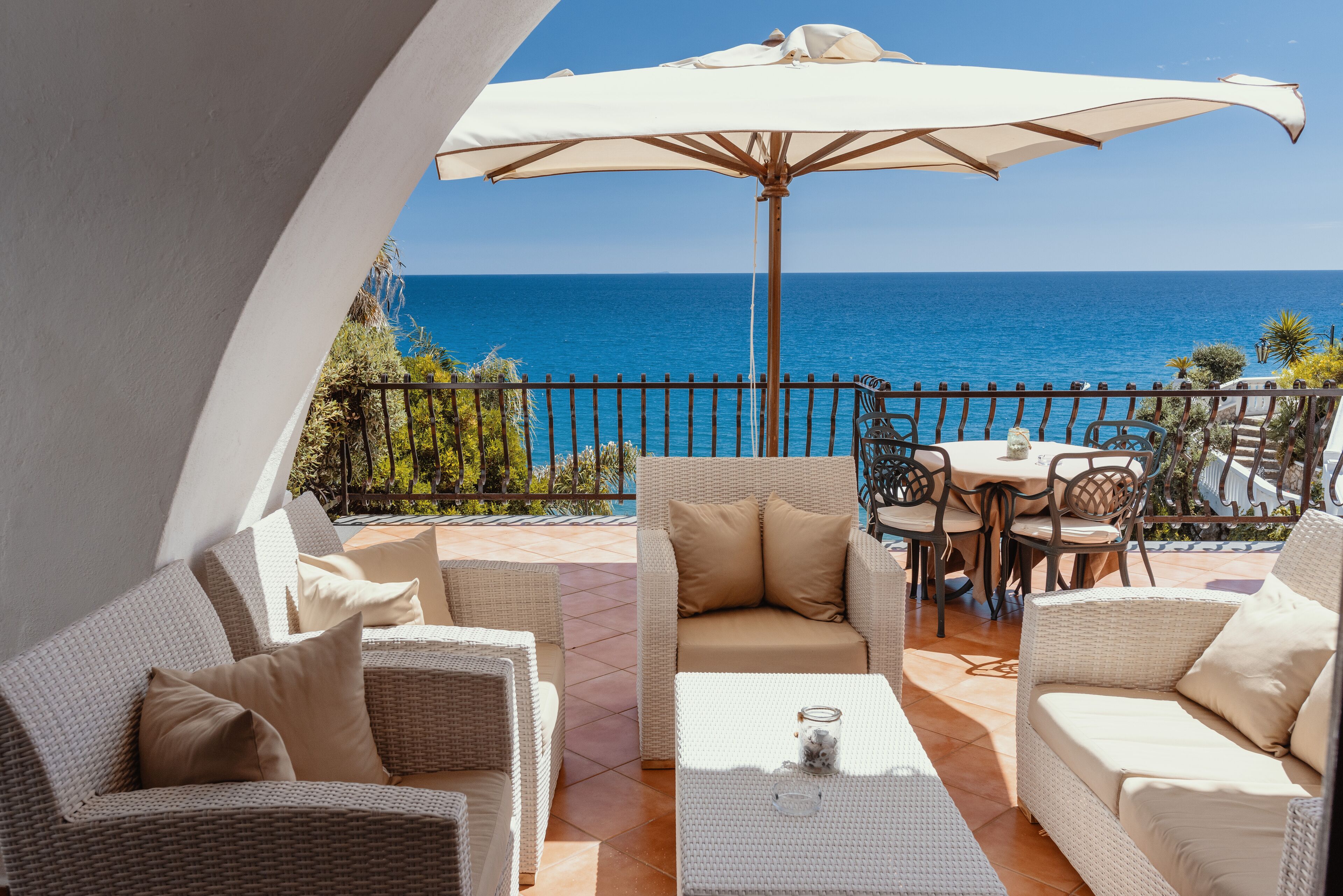 A balcony with wicker furniture, a table, and an umbrella, overlooking the sea.