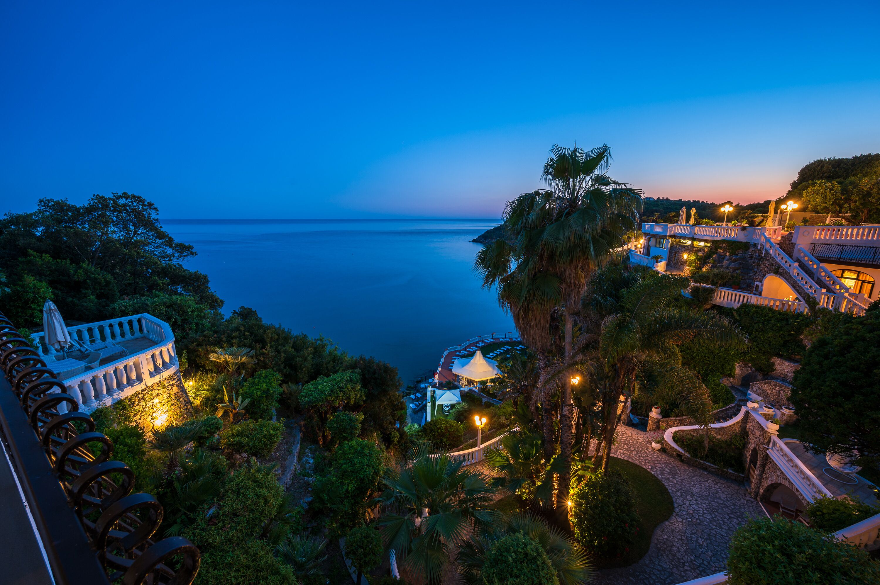 Un complejo turístico frente al mar, con un jardín ajardinado y un camino bien iluminado.