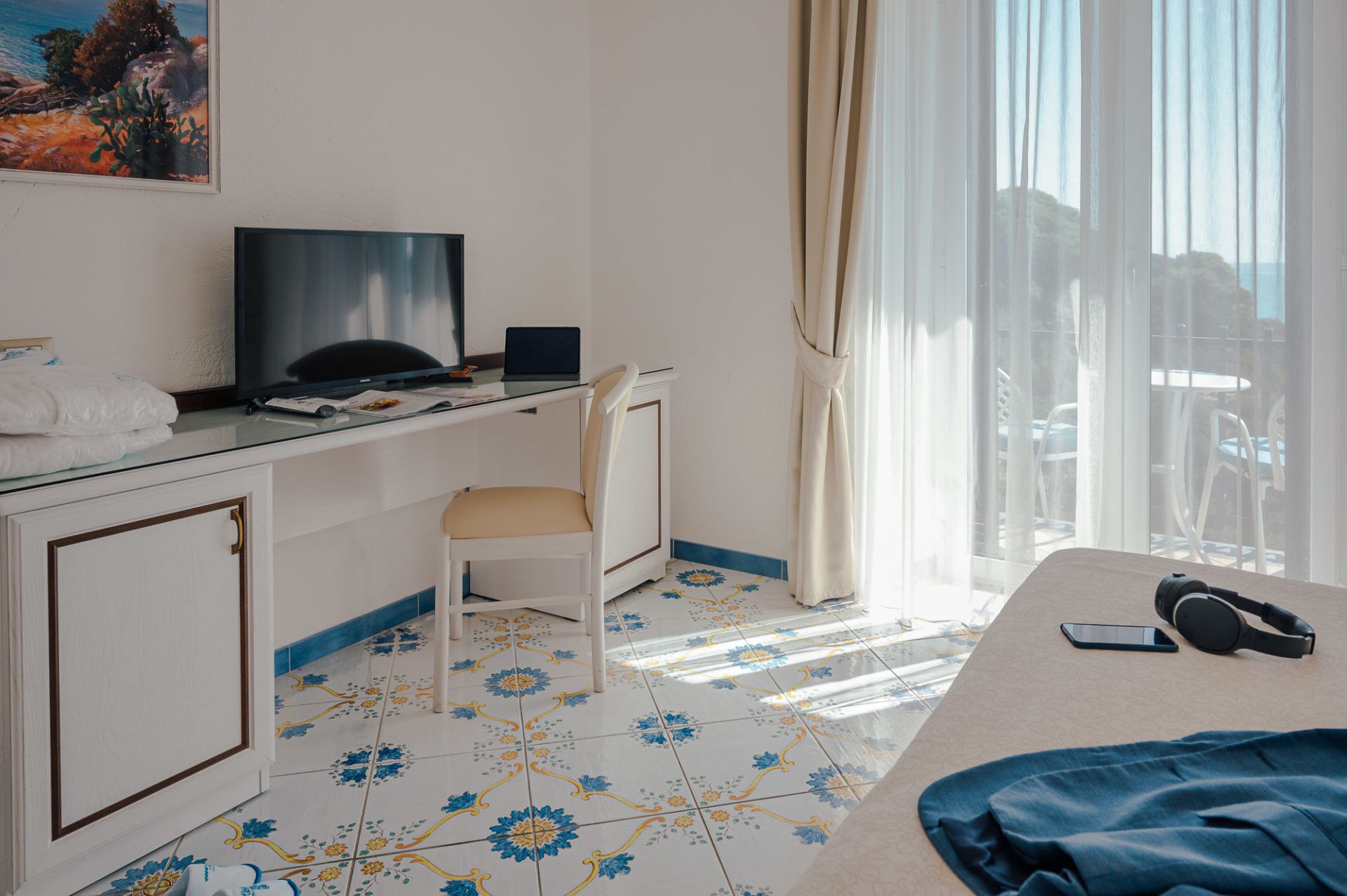 A hotel room with a bed, a desk with a laptop, a chair, and a television.