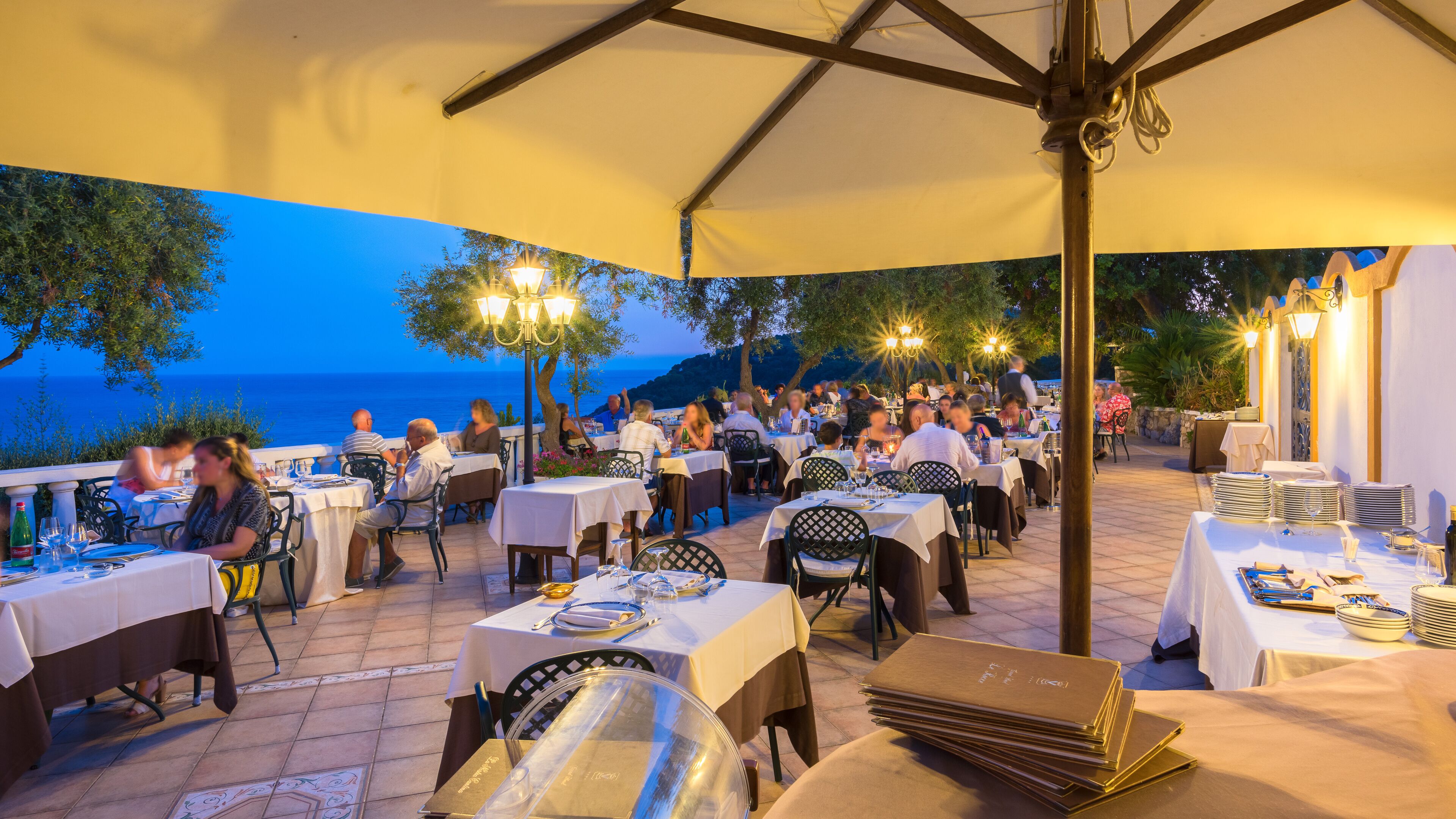 An outdoor dining area with tables and chairs, overlooking the sea.