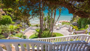 Un escalier menant à une terrasse offrant une vue sur la mer et un espace jardin aménagé avec des sièges d’extérieur.