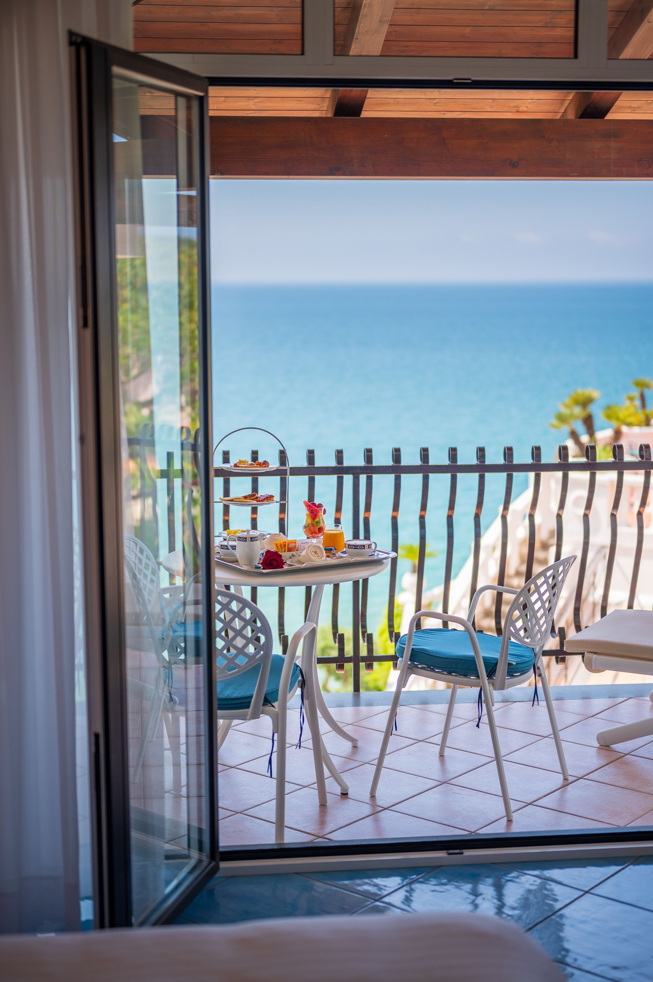 A balcony with a table set for breakfast, overlooking a coastal view.