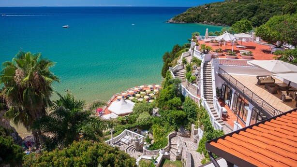 Un hôtel situé sur la côte, dot é d’une terrasse avec vue sur la mer, d’un espace piscine et d’une végétation luxuriante.