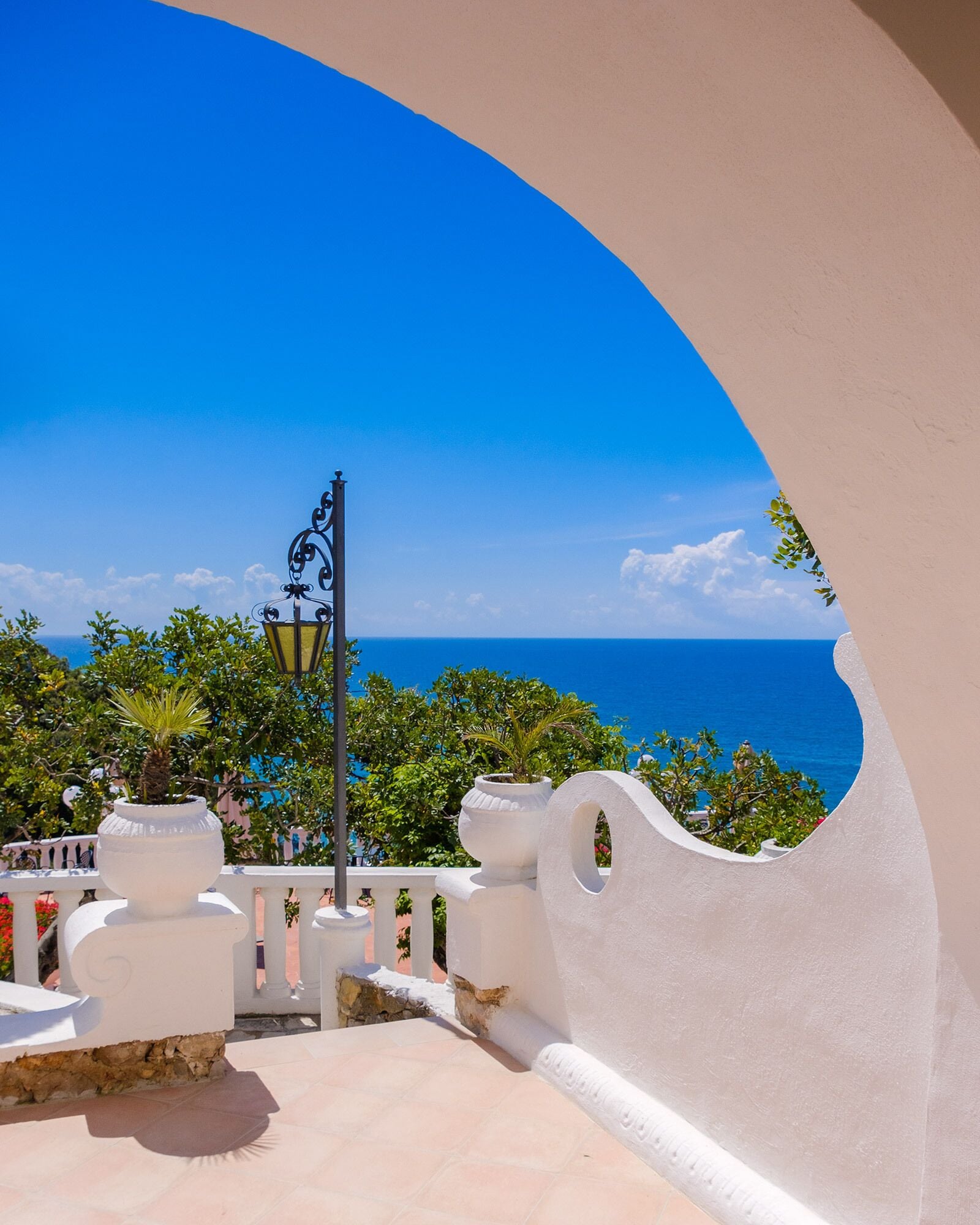 Une vue sur la côte depuis un balcon doté d’une balustrade blanche, d’une lampe décorative et de plantes en pot.