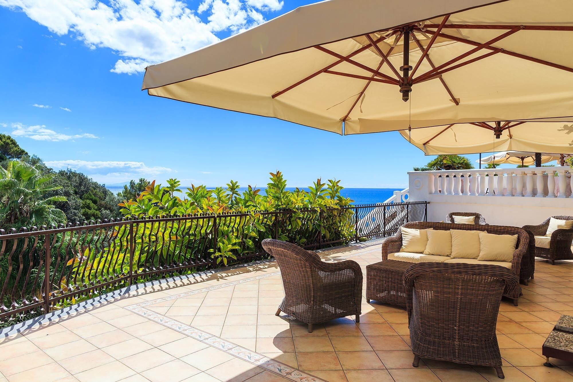 A terrace with wicker furniture, a large umbrella, and a view of the sea.
