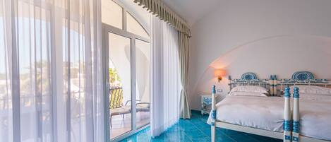 A bedroom with a bed, a nightstand, a lamp, and a view of a balcony.