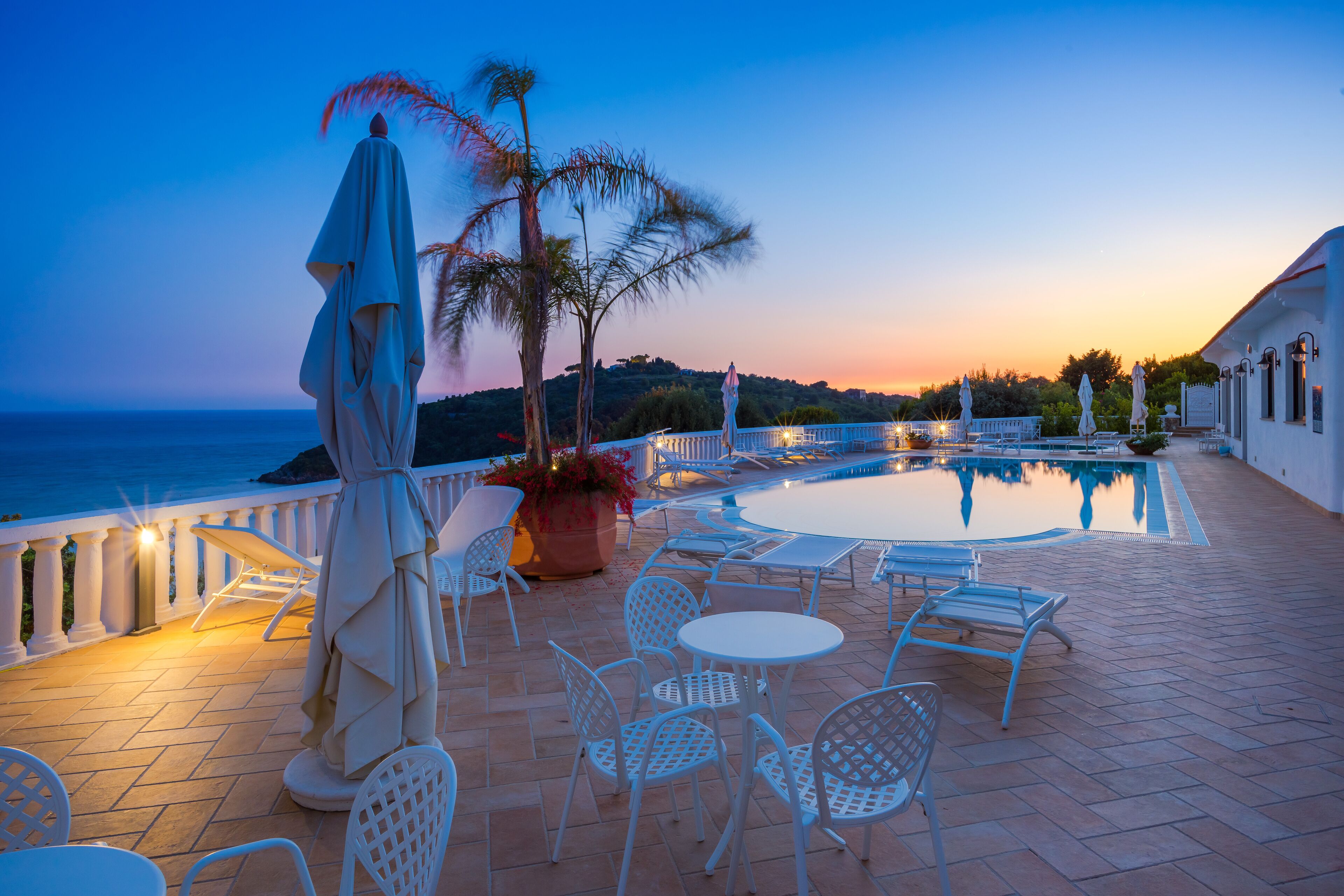 Un espace piscine aménagé sur le toit, avec des chaises longues, une table et une vue sur la mer au crépuscule.