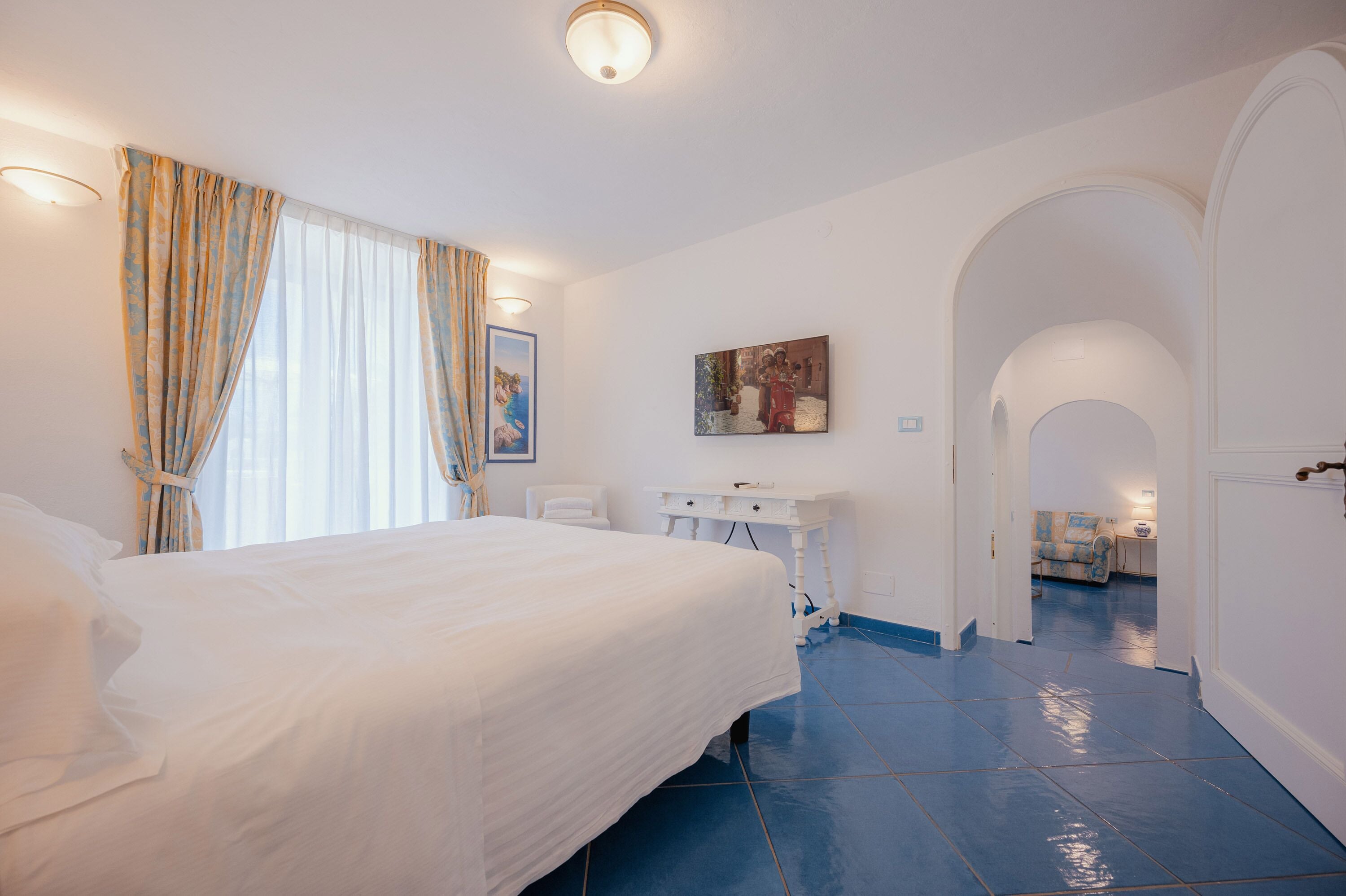 A hotel room with a large bed, a desk, and a painting on the wall.