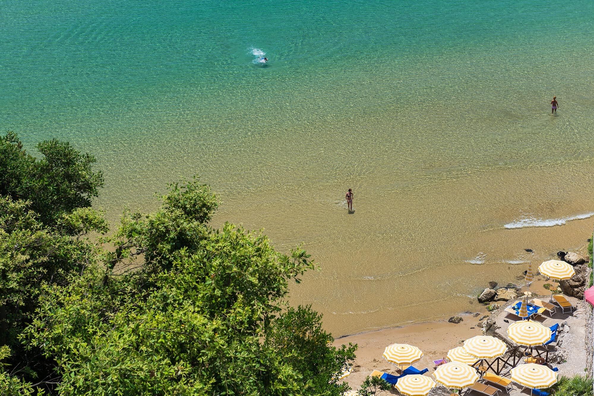 A beach with clear water, a few people, and beach umbrellas.