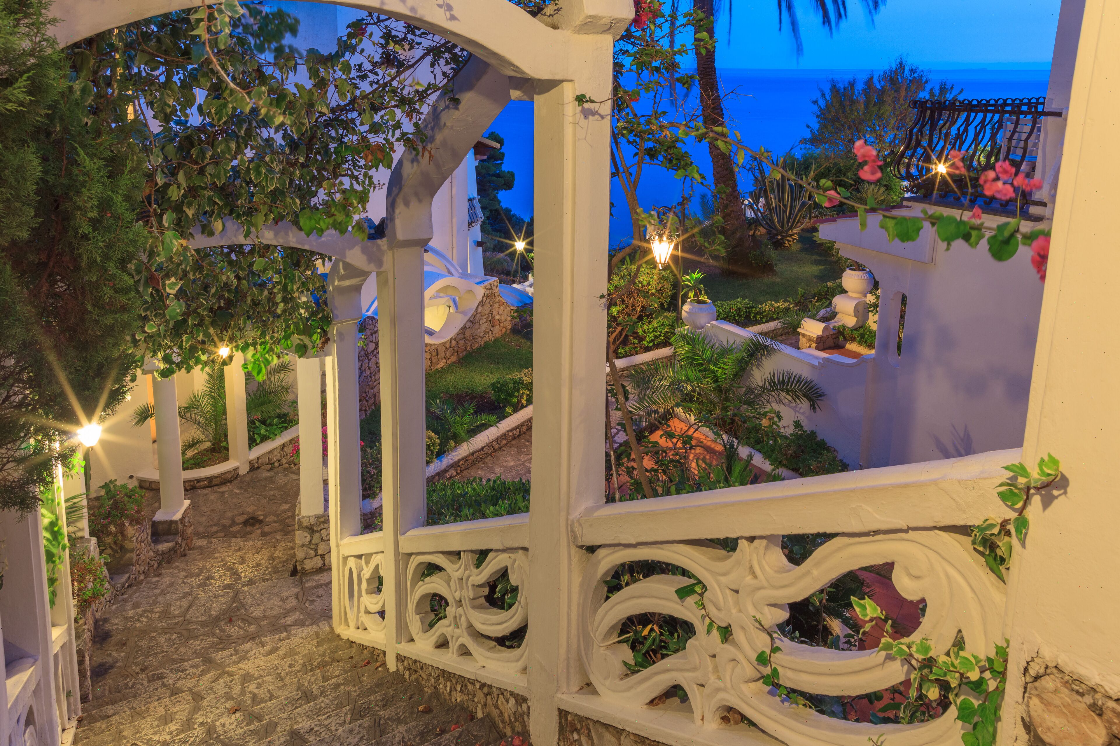 A white, ornate balcony with a stone pathway leading to a garden area.