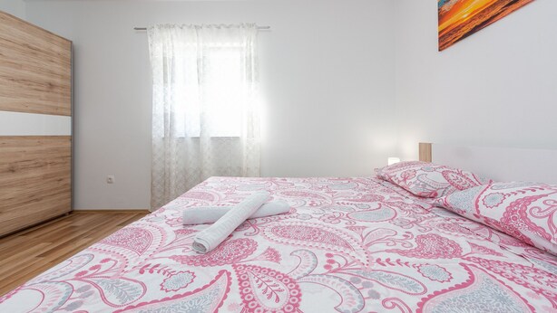 Ein Schlafzimmer mit Bett, einem Fenster mit Vorhängen, einem Bild an der Wand und einem Holzschrank.