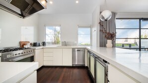 A modern kitchen with a gas stove, dishwasher, and a large window overlooking a cityscape. - Pet Friendly - Penthouse with City Views on Chapel (St Kilda)
