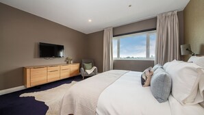 A modern hotel room with a large bed, a wooden dresser, a television mounted on the wall, and a window with curtains. - Pet Friendly - Penthouse with City Views on Chapel (St Kilda)
