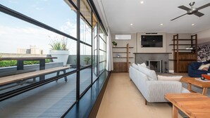 A modern living room with a sofa, coffee table, and a fireplace. There is a balcony with a view of the city. - Pet Friendly - Penthouse with City Views on Chapel (St Kilda)
