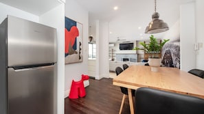 Une cuisine moderne avec un réfrigérateur en acier inoxydable, une table à manger en bois avec des chaises et un luminaire suspendu.