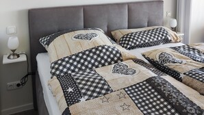 A neatly made bed with a checkered and polka dot duvet cover, a grey upholstered headboard, and a framed landscape painting above it. - Welcome to apartment 64 in house 1 of the Vier Jahreszeiten complex (Großenbrode)