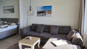 A modern living room with a grey sofa, a wooden coffee table, and a bed with patterned pillows. - Welcome to apartment 64 in house 1 of the Vier Jahreszeiten complex (Großenbrode)