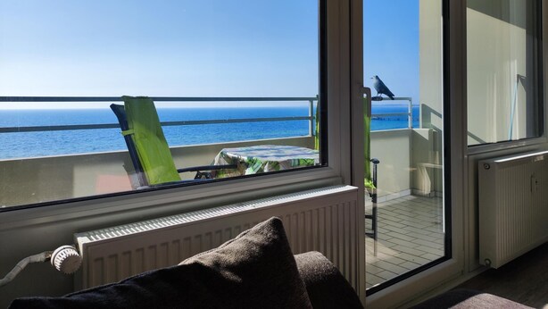 A balcony with a view of the sea, a chair, a table, and a radiator. - Welcome to apartment 64 in house 1 of the Vier Jahreszeiten complex (Großenbrode)