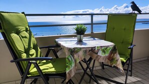 A balcony with two green cushioned chairs, a small table with a plant, and a view of the sea. - Welcome to apartment 64 in house 1 of the Vier Jahreszeiten complex (Großenbrode)