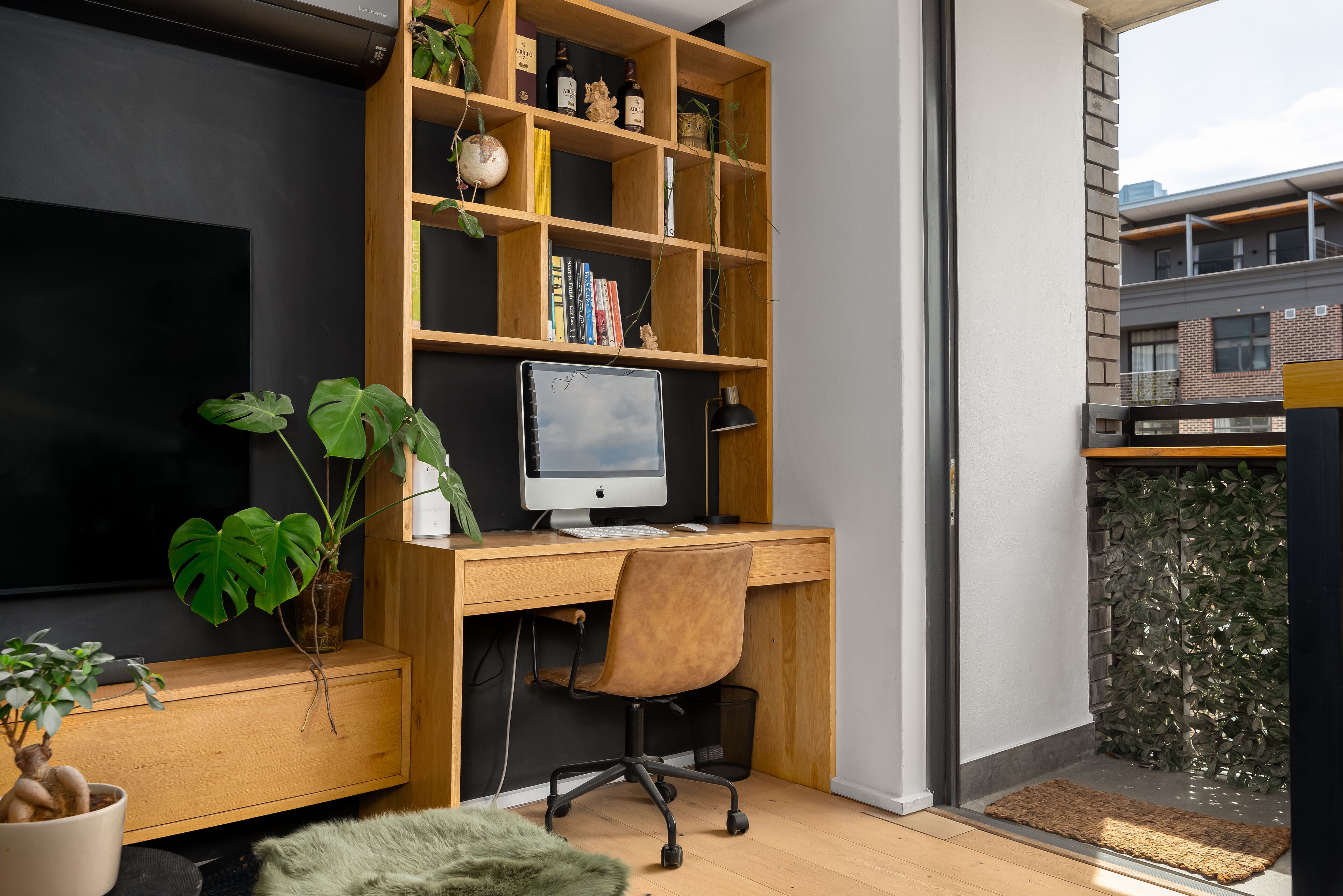 A modern workspace with a wooden desk, computer, and bookshelf.