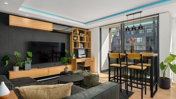 A modern living room with a flat-screen TV, wooden shelving, a dining area with chairs, and potted plants.