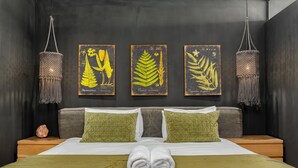 A neatly made bed with green and white bedding, two green pillows, and a pair of towels on a green bed runner. There are three framed botanical illustrations on the wall above the bed. - The Iron Works 611 (Cape Town)