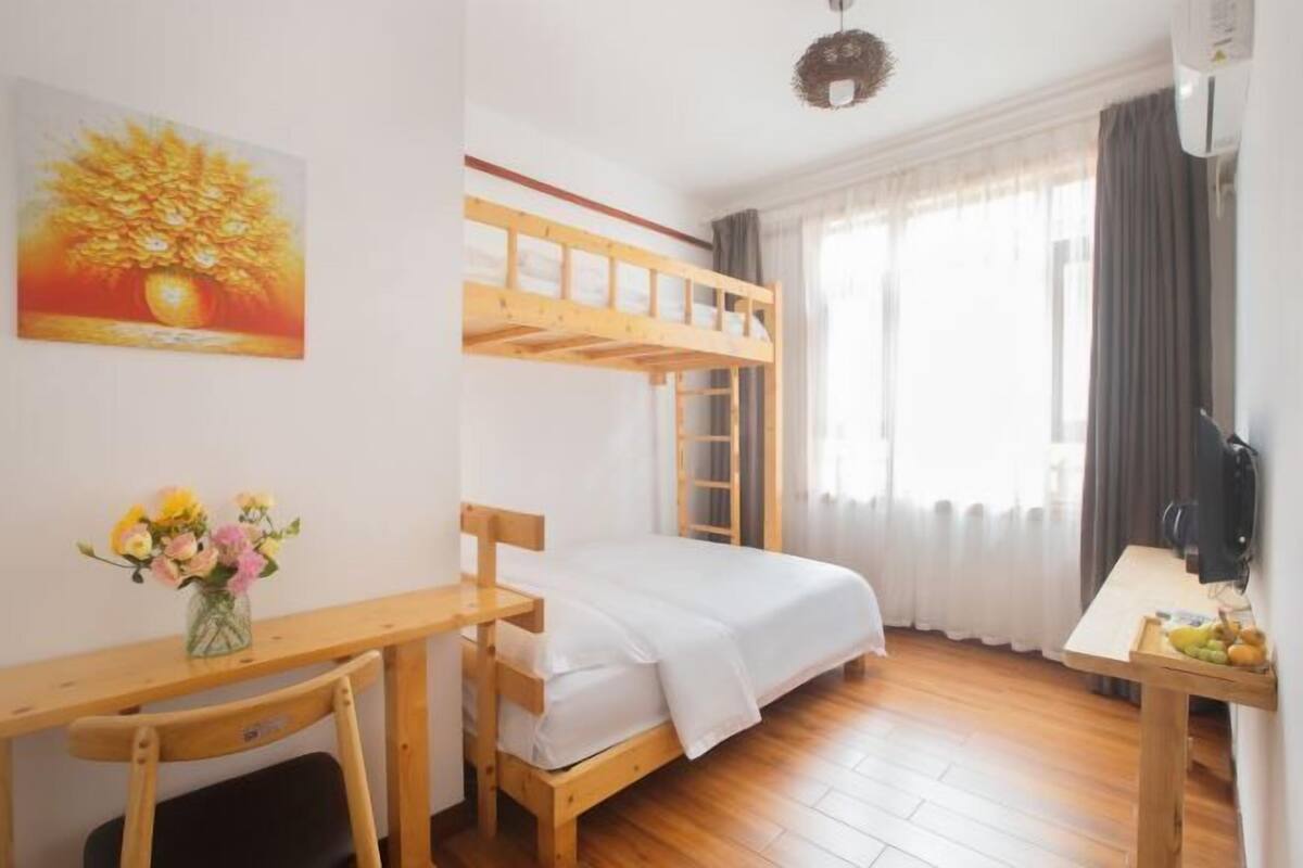 A room with a bunk bed, a desk with a chair, a vase of flowers, and a television.