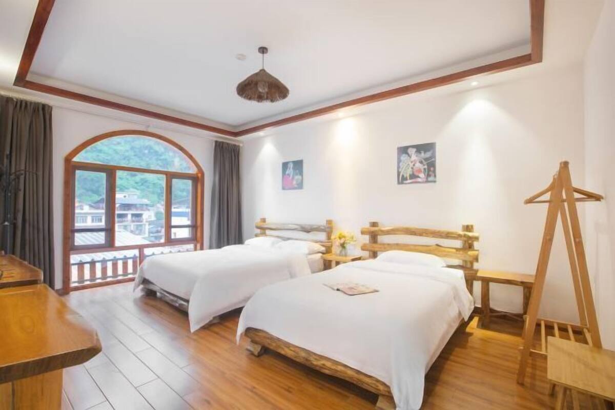A room with two beds, wooden flooring, a large window, and a wooden ceiling.