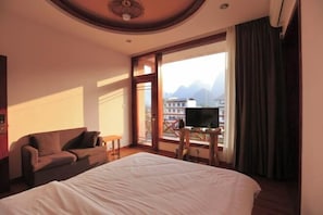 Habitació d'hotel amb un llit gran, un sofà, una televisió sobre un suport de fusta, i un balcó amb vista a les muntanyes.