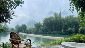 A chair and a stone table by a river with a view of mountains and greenery. - Xiaolonghe Hotel (Yangshuo Yulonghe Scenic Area) (Yangshuo)