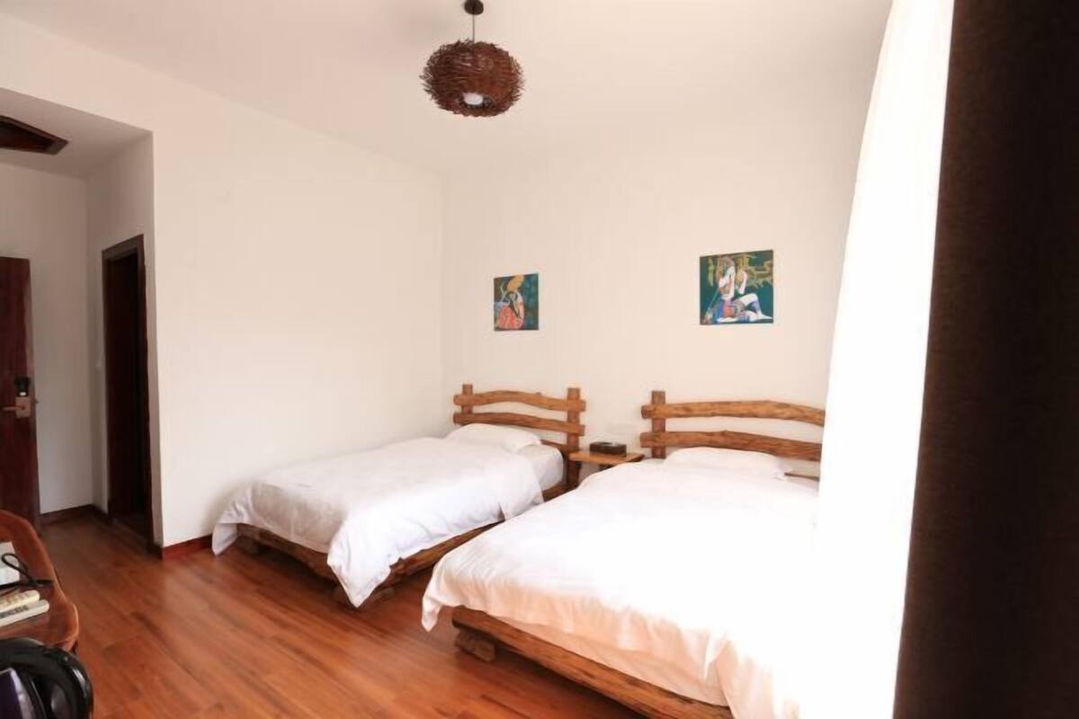 A room with two wooden beds, a woven ceiling light, and two small paintings on the wall.