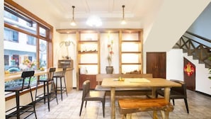 A dining area with a wooden table and chairs, a bar area with stools, and a view of the outside through large windows. - Xiaolonghe Hotel (Yangshuo Yulonghe Scenic Area) (Yangshuo)