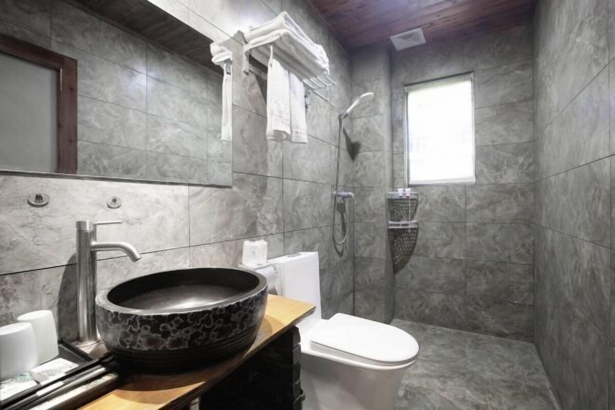 A modern bathroom with a large basin sink, a toilet, and a shower.