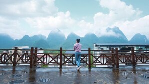 A person standing on a wet platform overlooking a mountainous landscape. - Xiaolonghe Hotel (Yangshuo Yulonghe Scenic Area) (Yangshuo)