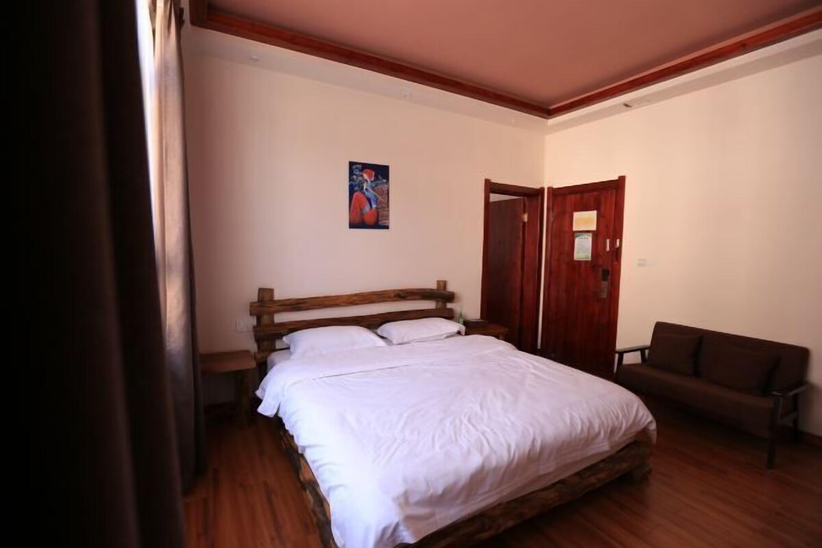 A bedroom with a wooden bed, a wooden bench, a brown sofa, and a door.