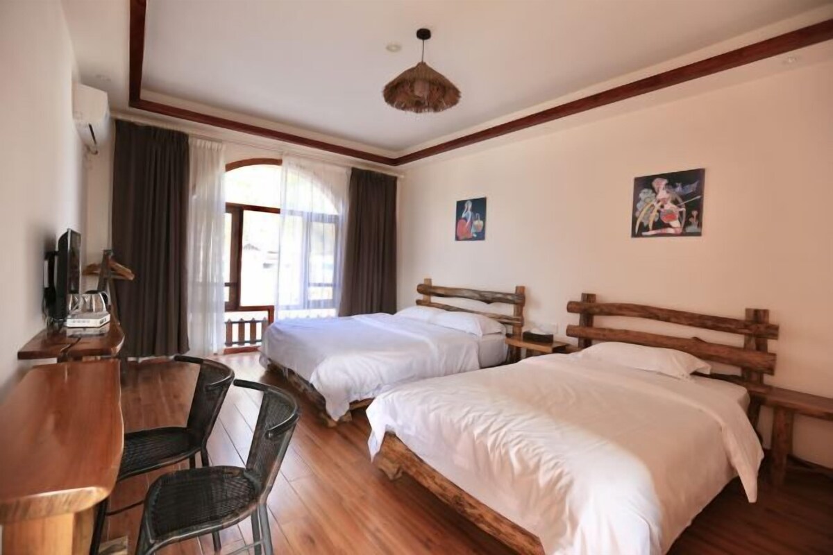 A room with two wooden beds, a wooden table with chairs, a ceiling fan, and a window with curtains.