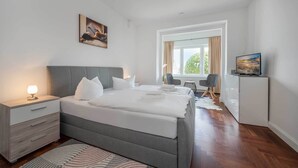 A modern bedroom with a large bed, bedside tables, a desk, and a TV. - Villa Meereswoge 02 - directly on the pier (Bansin (Seebad))