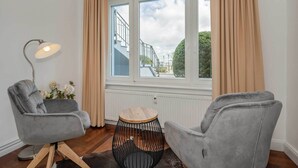 A room with two grey armchairs, a small round wooden table, a floor lamp, and a window with curtains. - Villa Meereswoge 02 - directly on the pier (Bansin (Seebad))