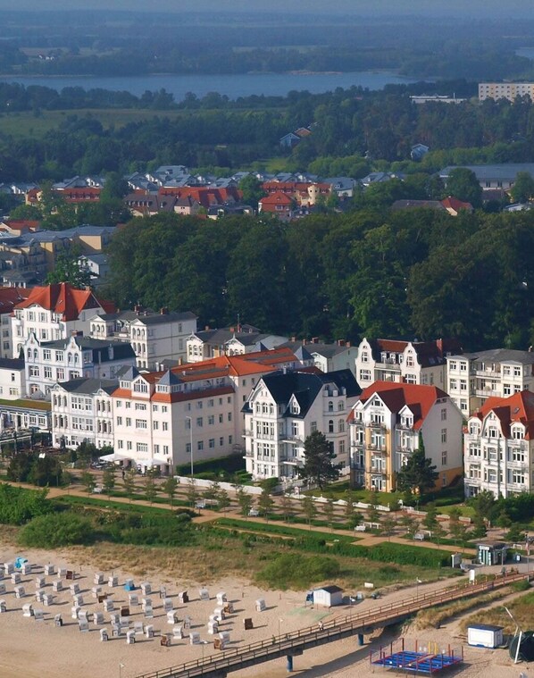 A coastal town with historic buildings, a beach with sun loungers, and a bridge connecting the area.