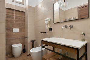A modern bathroom with a wooden vanity, a toilet, a bidet, and a hairdryer mounted on the wall. - 3251 Dellatita Suite by Barbarhouse (Lecce)
