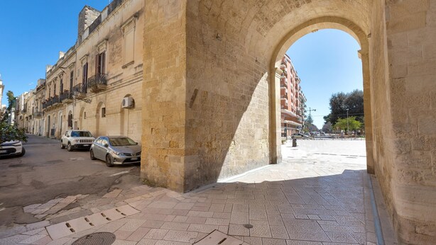 A stone archway leading to a paved street with parked cars and buildings on either side.