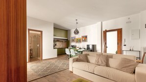 A modern living room with a beige sofa, a green ottoman, and a dining area with a glass door leading to a kitchen.