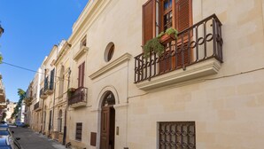 A row of traditional buildings with balconies, a street, and parked cars.